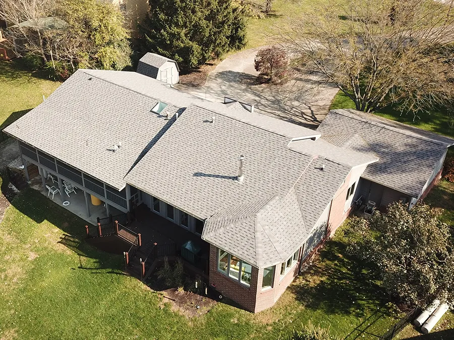 Overhead view of a house with a gray shingled roof, lawn, and surrounding trees.