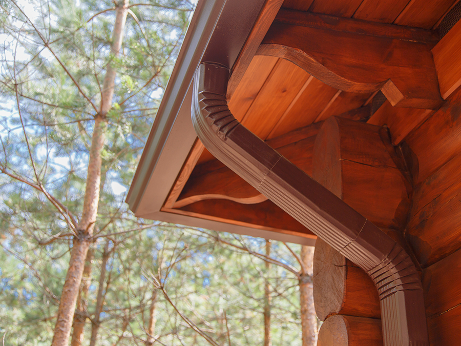 A close up of a wooden house with a gutter and trees in the background.