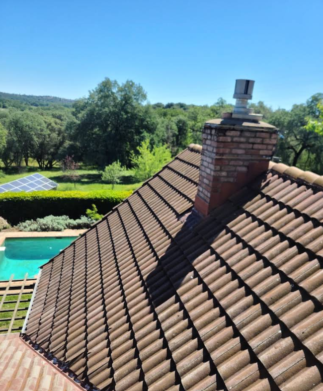 Terracotta-tiled roof with brick chimney overlooking a pool and green countryside under a blue sky