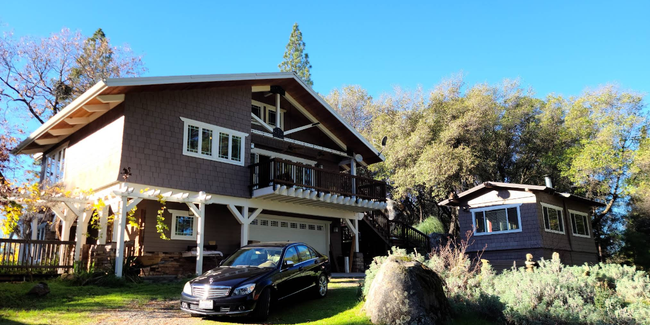 Two-story house with a balcony and parked car on a sunny wooded hillside