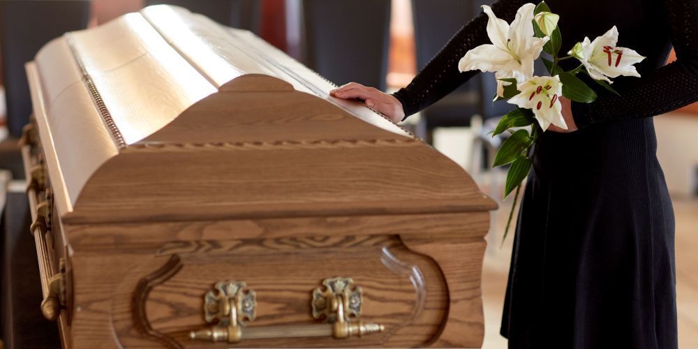 Person holding white lilies beside a wooden casket during a memorial service at a funeral home and cremations provider in Annetta, TX