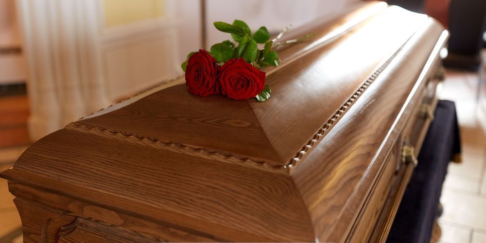Wooden funeral casket with red roses placed on top during a memorial service at a funeral home and cremations provider in Weatherford, TX