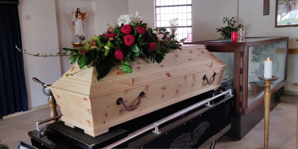 Funeral viewing with a light wooden casket and floral arrangement inside a chapel at a funeral home and cremations provider in Weatherford, TX