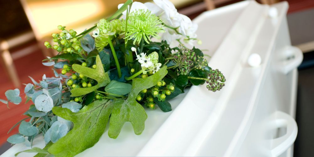 Green and white floral arrangement placed on a white casket at a service by a funeral home and cremations in Hudson Oaks, TX