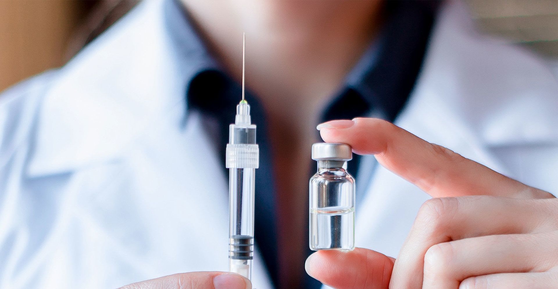 Person holding a syringe and vial of clear liquid, likely for injection.