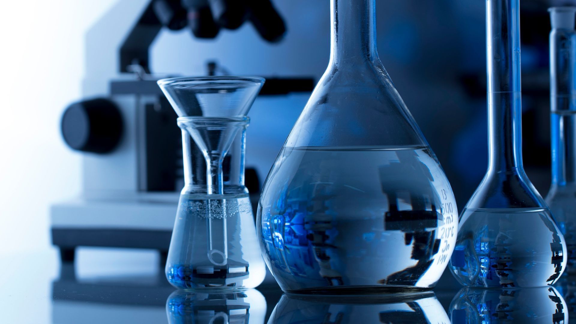 Laboratory glassware with liquid inside, and a microscope, all in blue tones.
