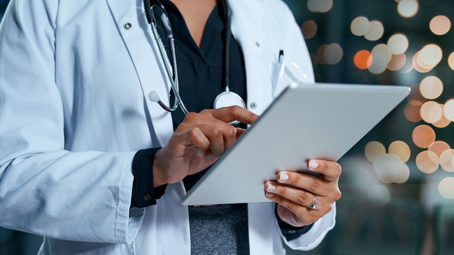 Doctor in white coat using a tablet with stethoscope around neck.