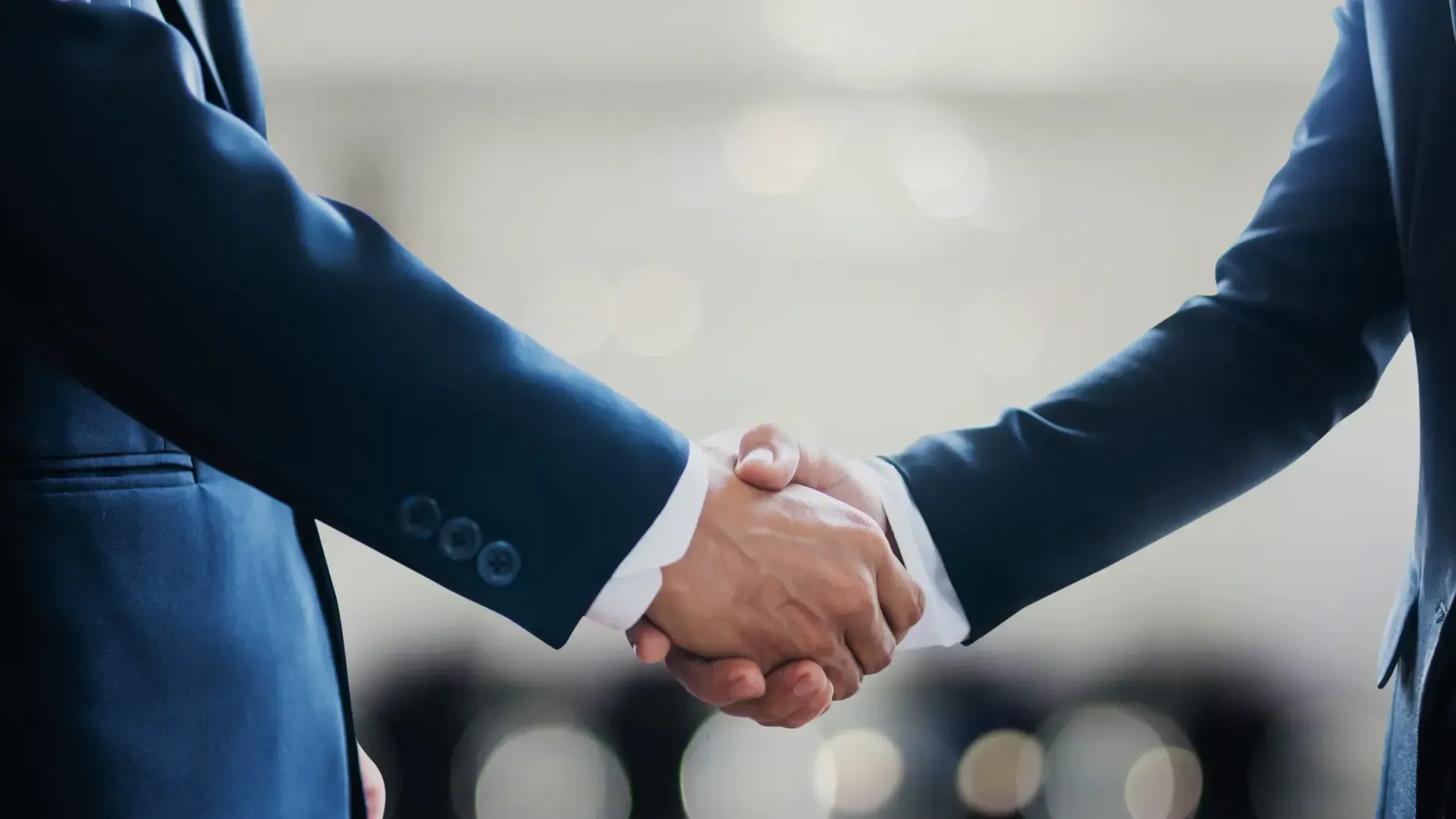 Two men in suits are shaking hands in a room.