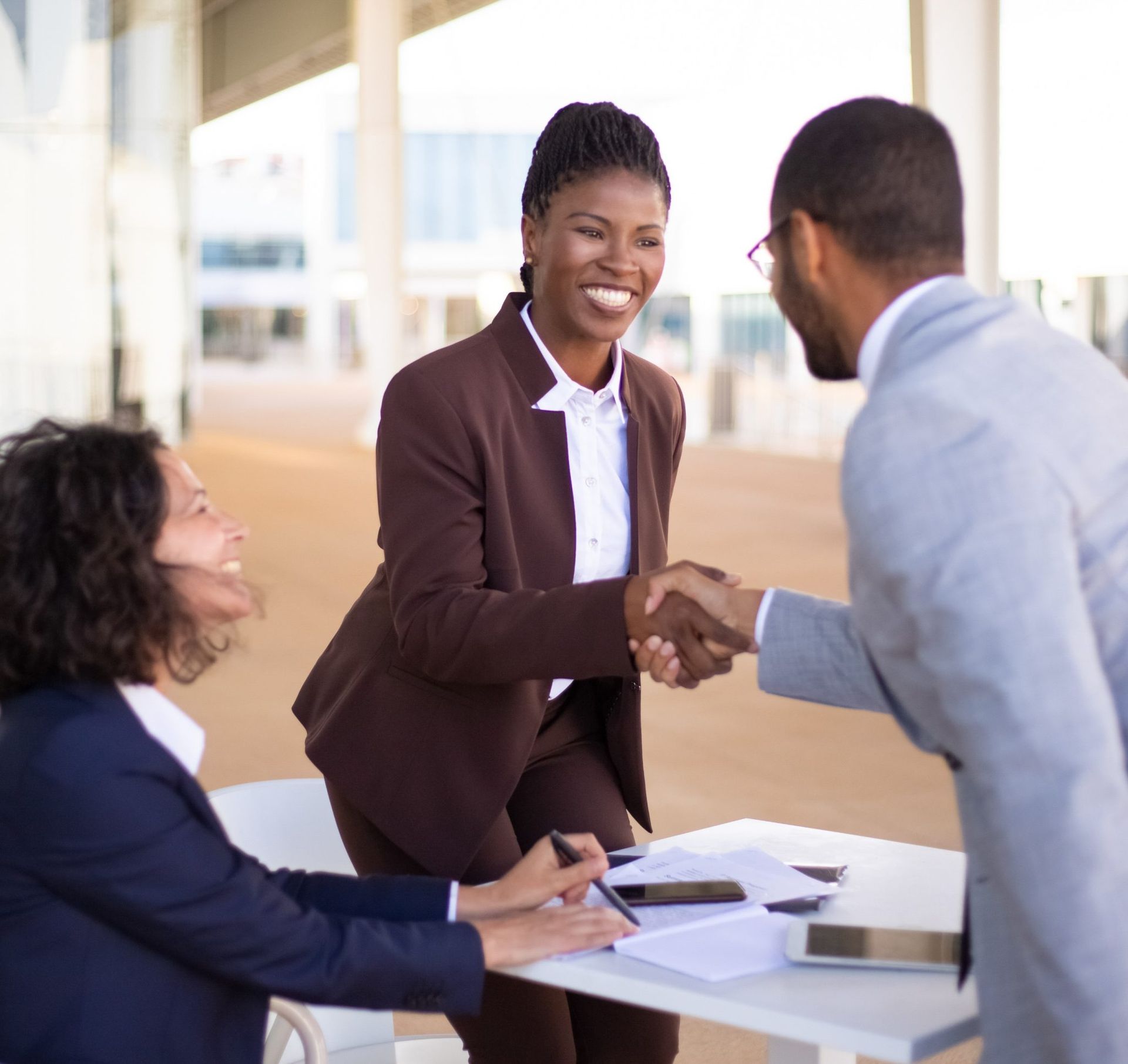 A woman in a brown suit is shaking hands with a man in a gray suit.
