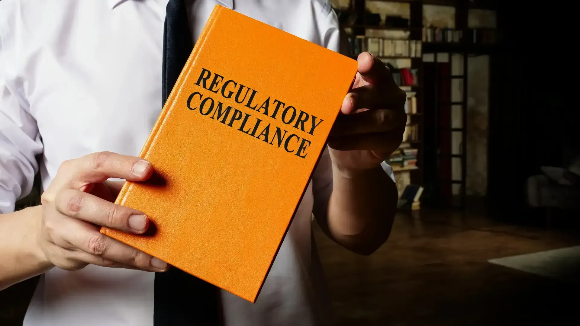 A man is holding an orange book titled regulatory compliance.