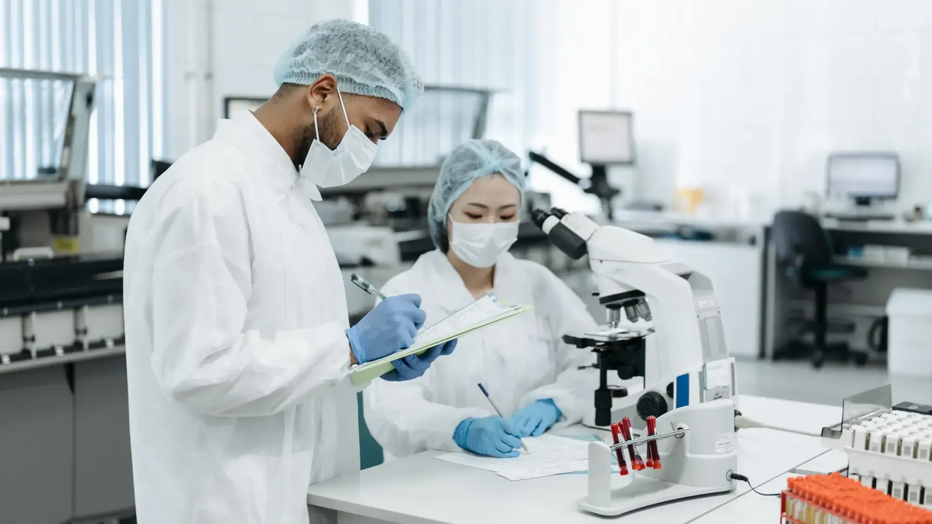 Two scientists are working in a laboratory with a microscope and a clipboard.