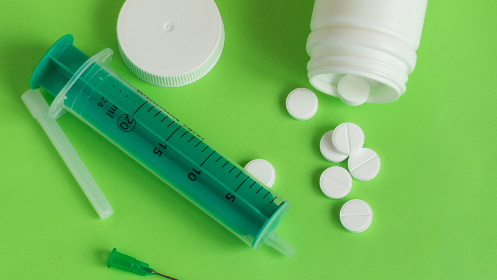 A syringe , needle , bottle and pills on a green surface.
