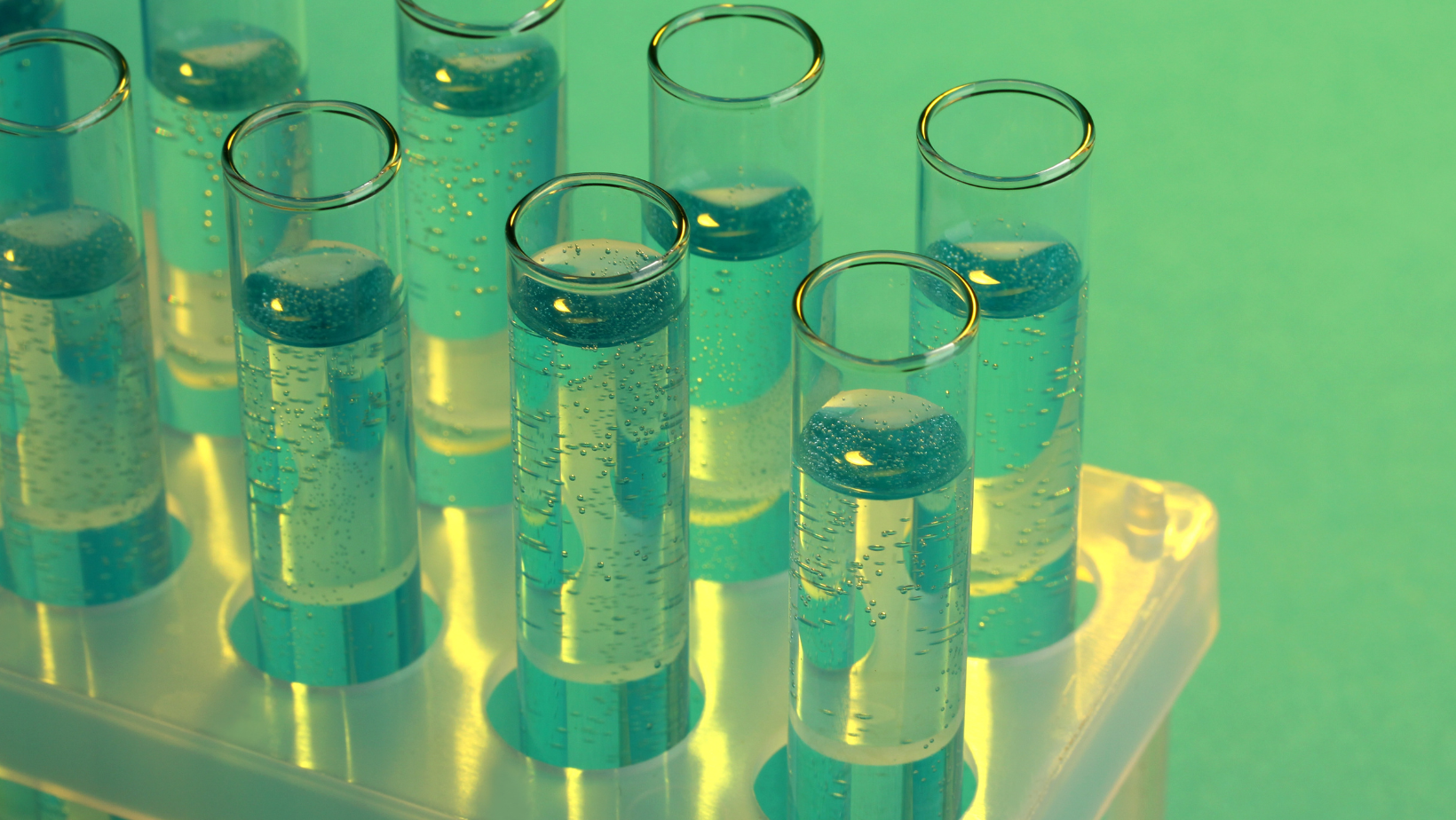 A tray of test tubes filled with blue liquid on a green surface.