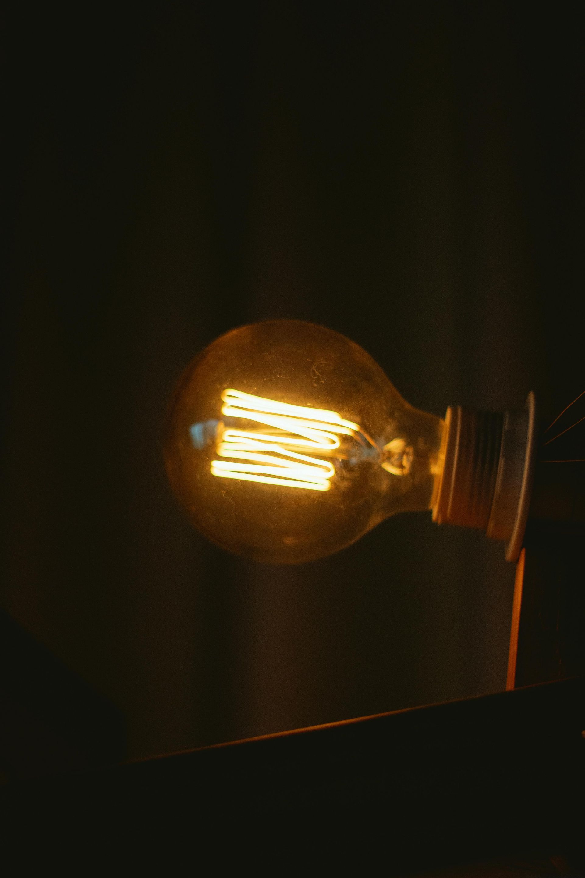 Glowing Edison-style lightbulb in a dark setting, emitting warm light.