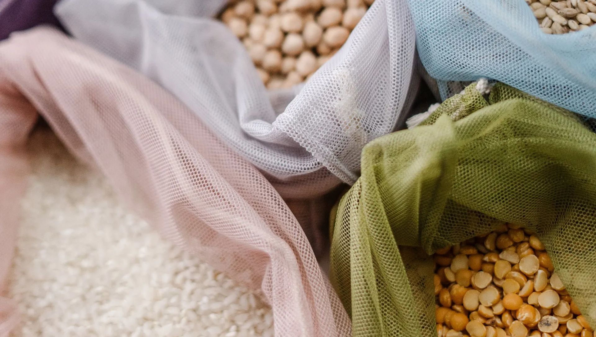 Bags of grains and legumes: chickpeas, rice, peas. Multicolored mesh bags in close-up.