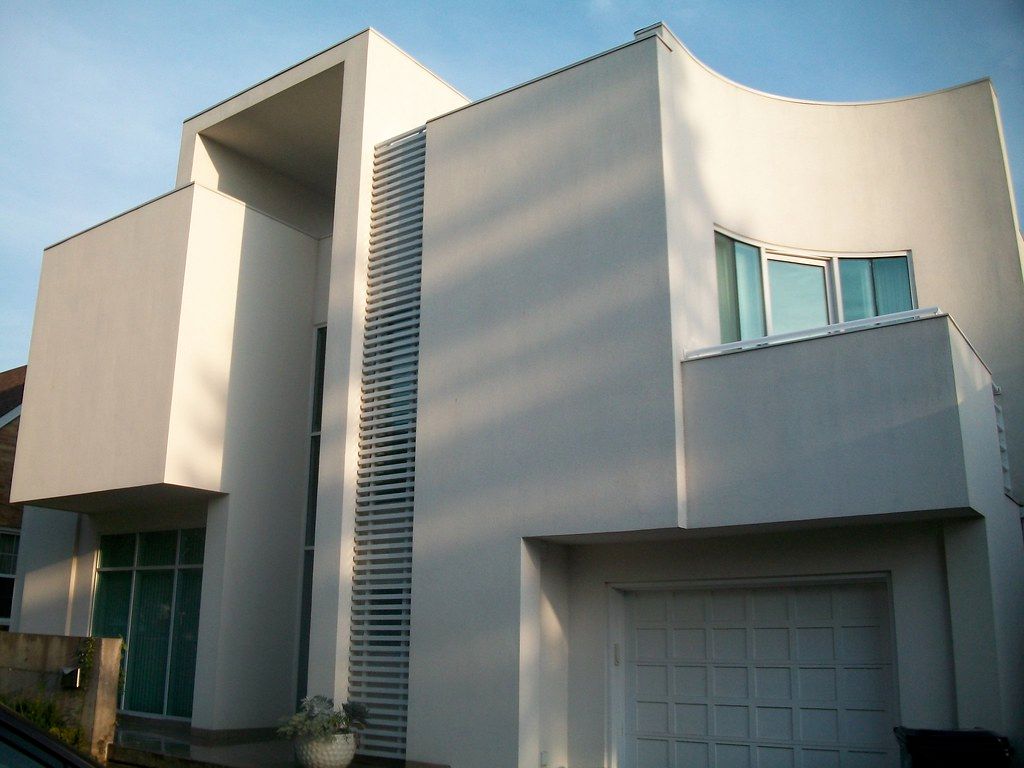 Modern white house with curved and rectangular sections, a garage, and large windows.