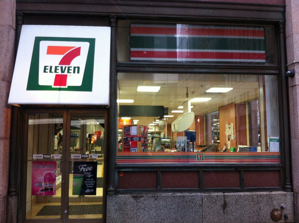 7-Eleven storefront with illuminated logo and red, green, and orange stripes.