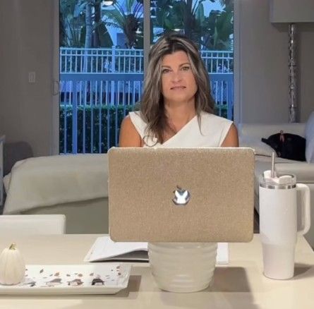 Kristy Realtor seated at a table with a laptop, looking at the camera in a bright home interior.