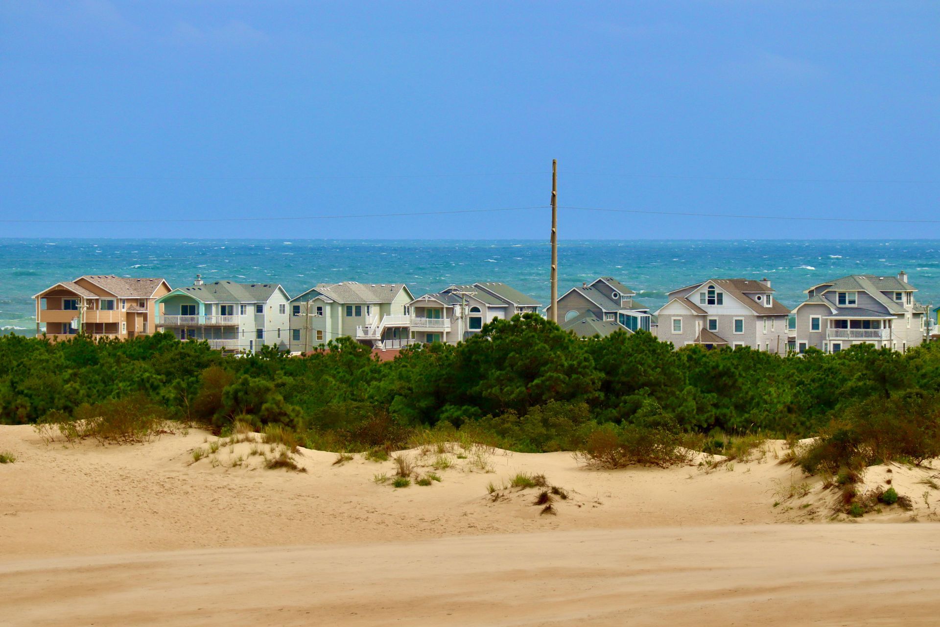 Beachfront houses behind sand dunes under a clear blue sky