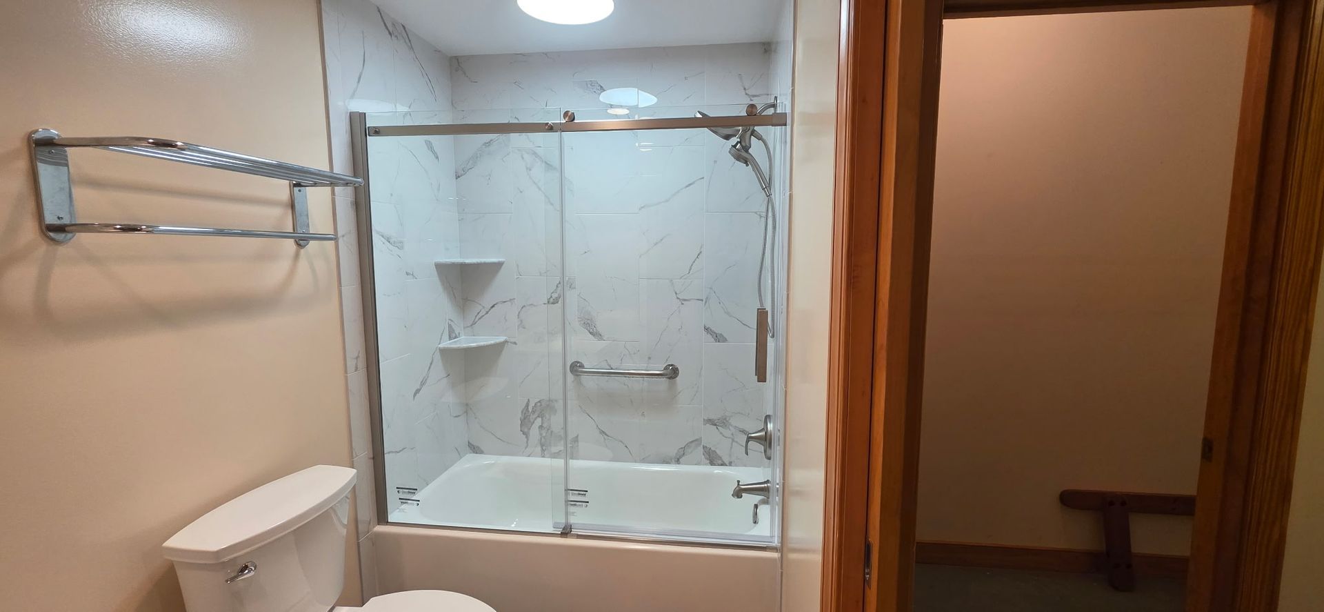 Bathroom with glass shower enclosure, towel rack, toilet, and doorway to a lit room