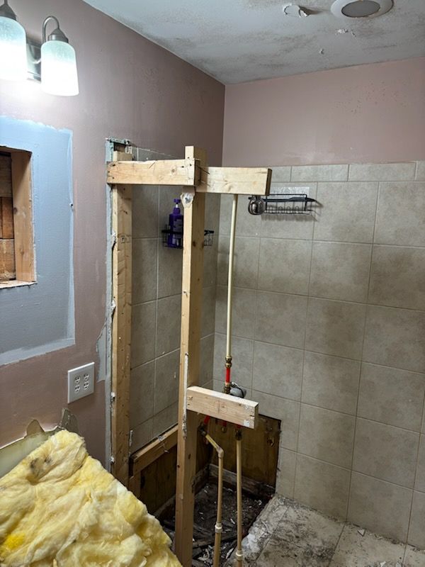 Partially tiled bathroom under renovation with exposed shower framing and insulation on the floor