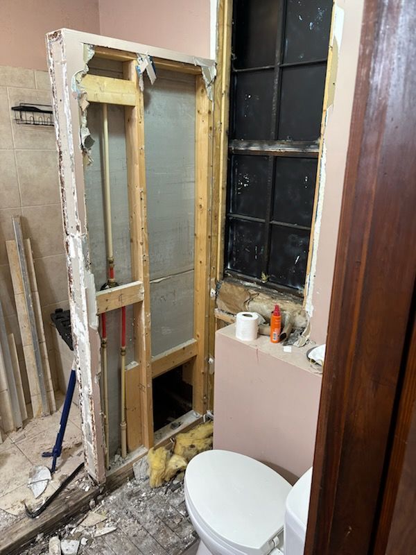 Bathroom under renovation with exposed wall studs, debris, toilet, and a window opening.