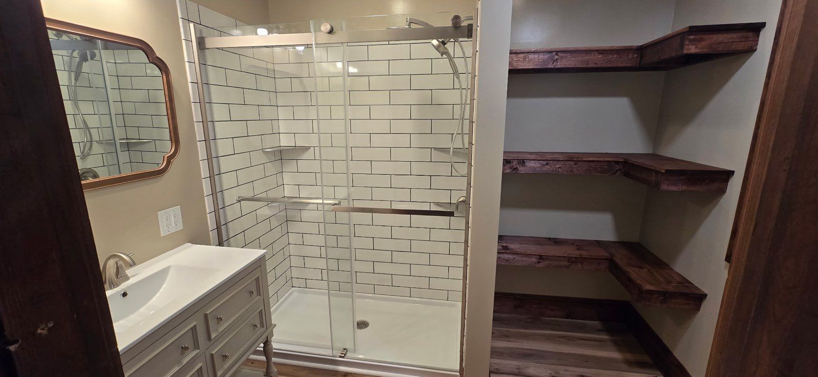 Bathroom with tiled shower, vanity, mirror, and open shelving units on either side.