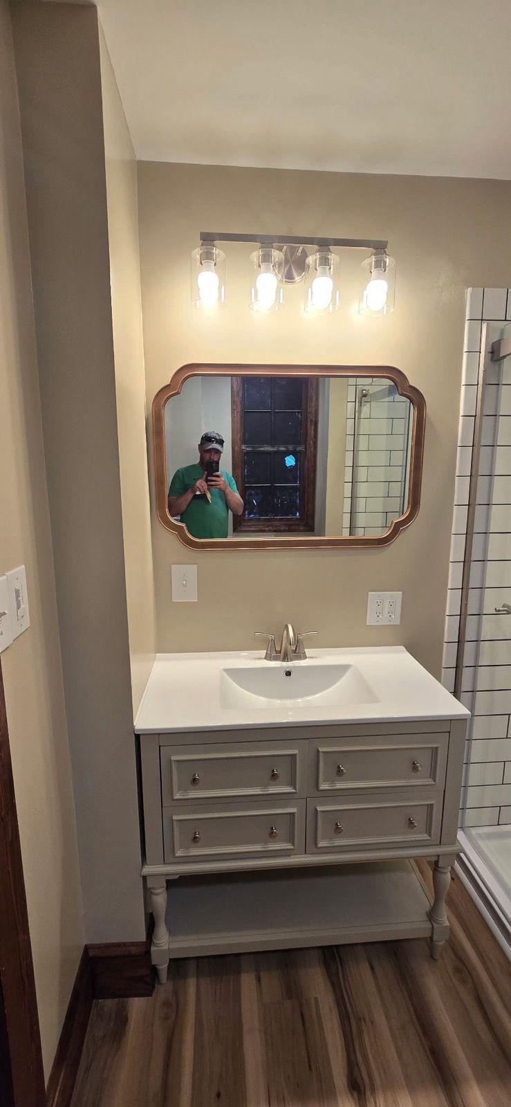 Bathroom vanity with mirror, white sink, gray drawers, and warm light fixture in a narrow room