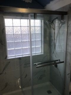 Glass shower stall with frosted window and chrome grab bar in a bathroom