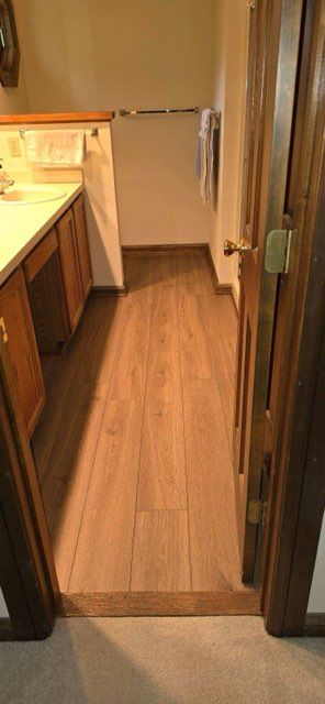 Narrow kitchen doorway with wood flooring leading into a small room with cabinets and a sink counter.