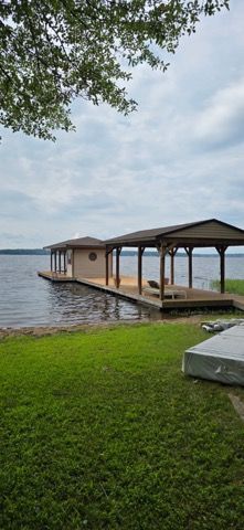 Lakeside dock with covered gazebo and green lawn under a cloudy sky