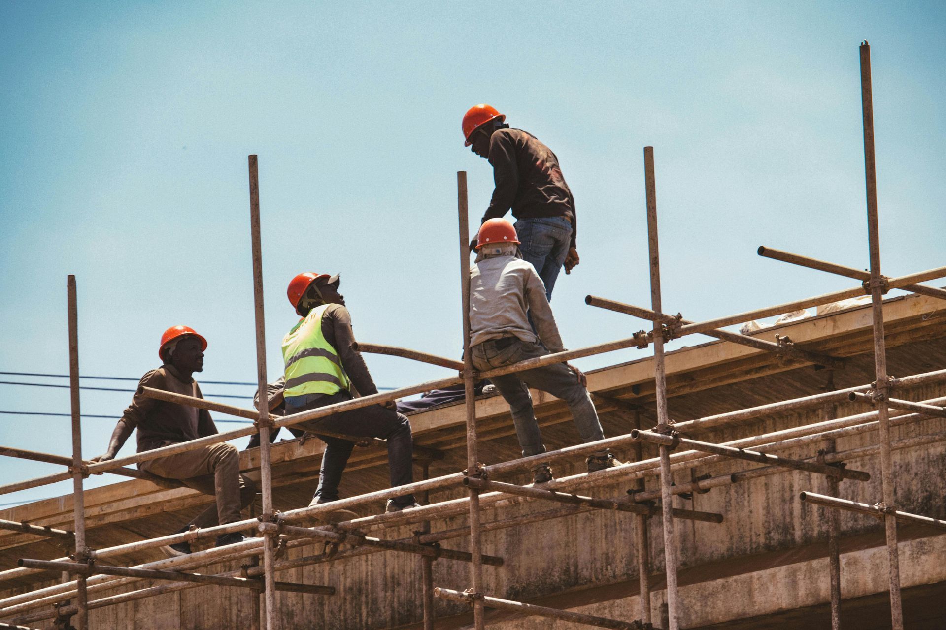Construction workers on scaffolding installing beams on a building roof under a clear sky