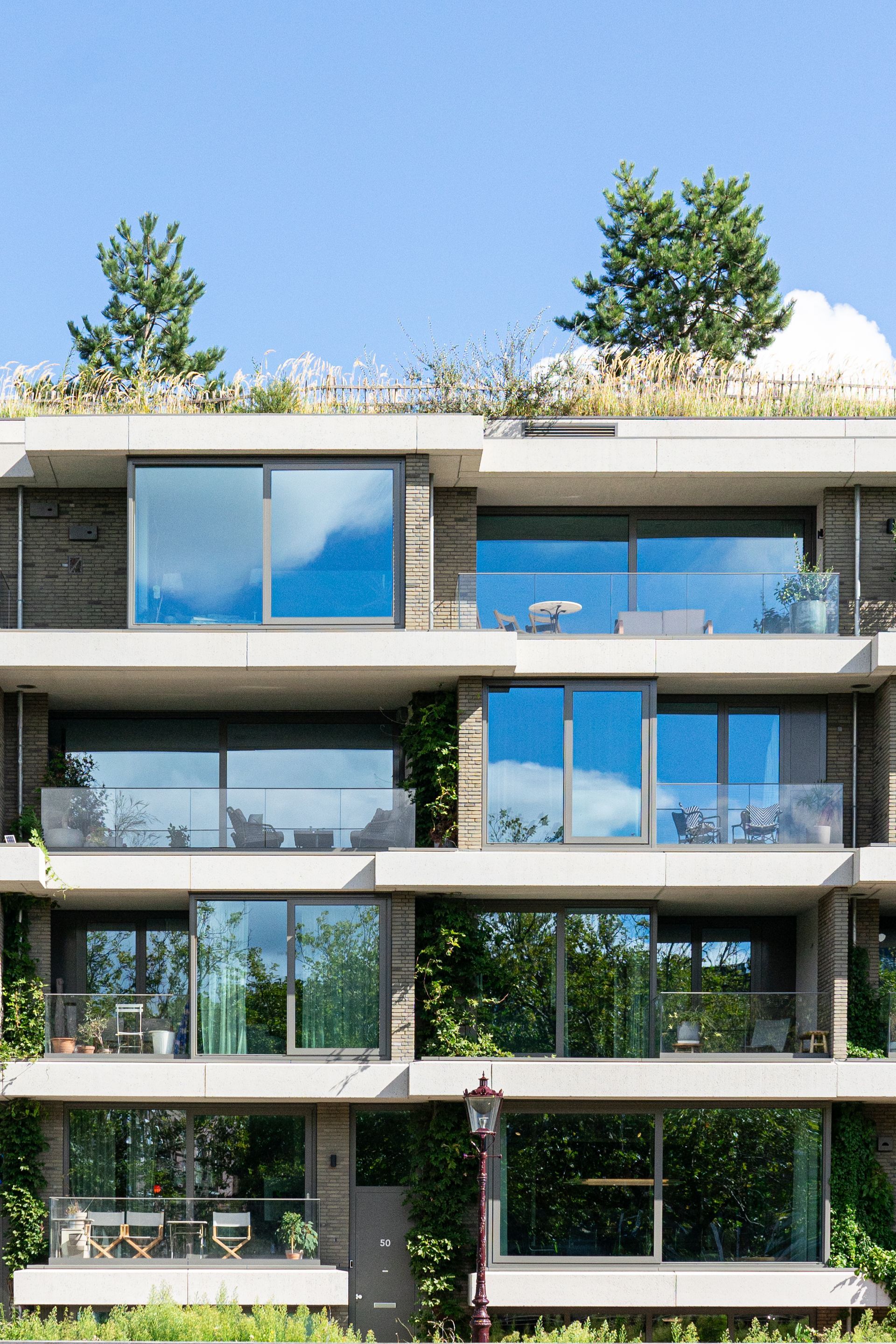 Modern apartment building with glass balconies and rooftop greenery against a blue sky