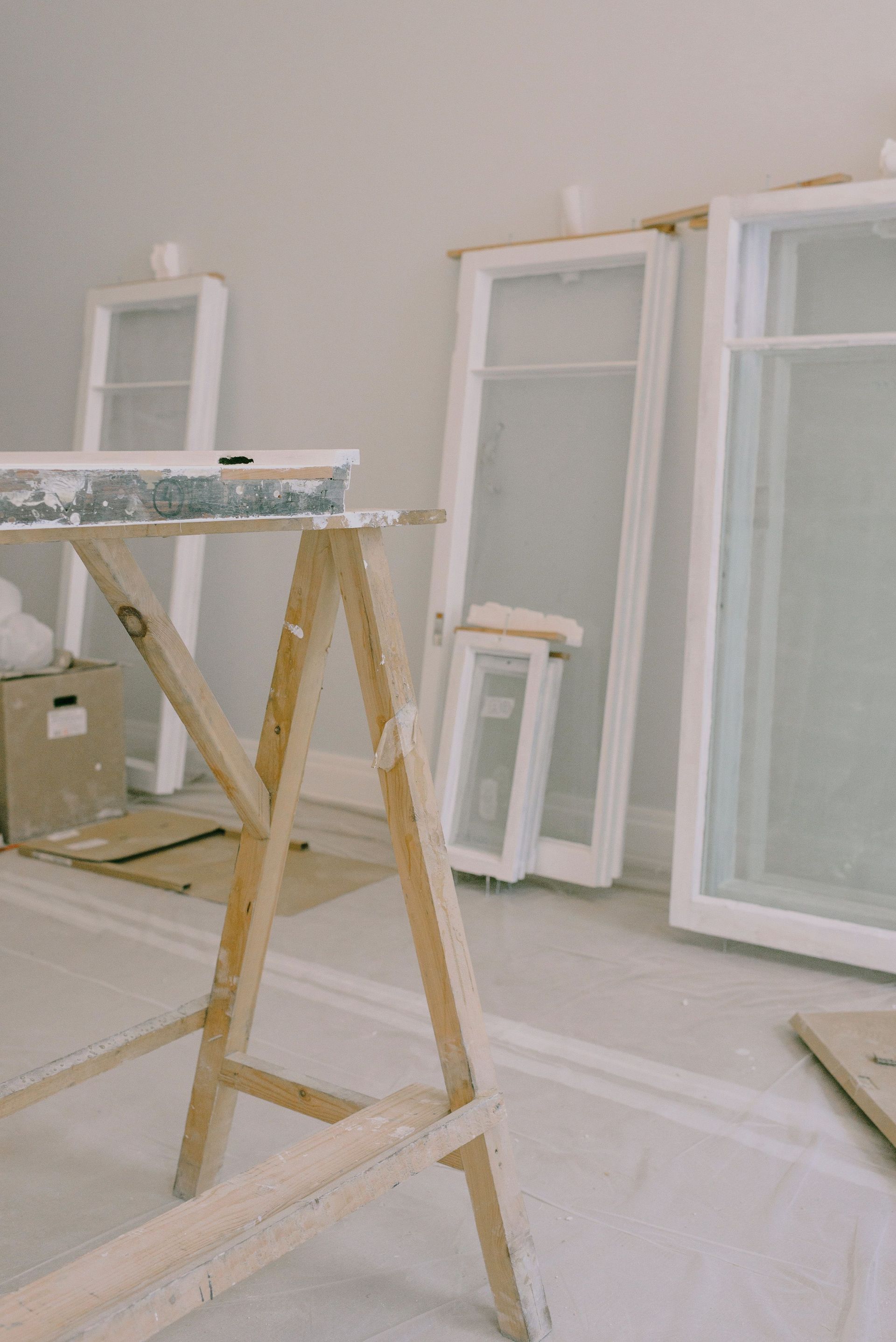 Renovation room with sawhorse, leaning window frames, and dust-covered floor