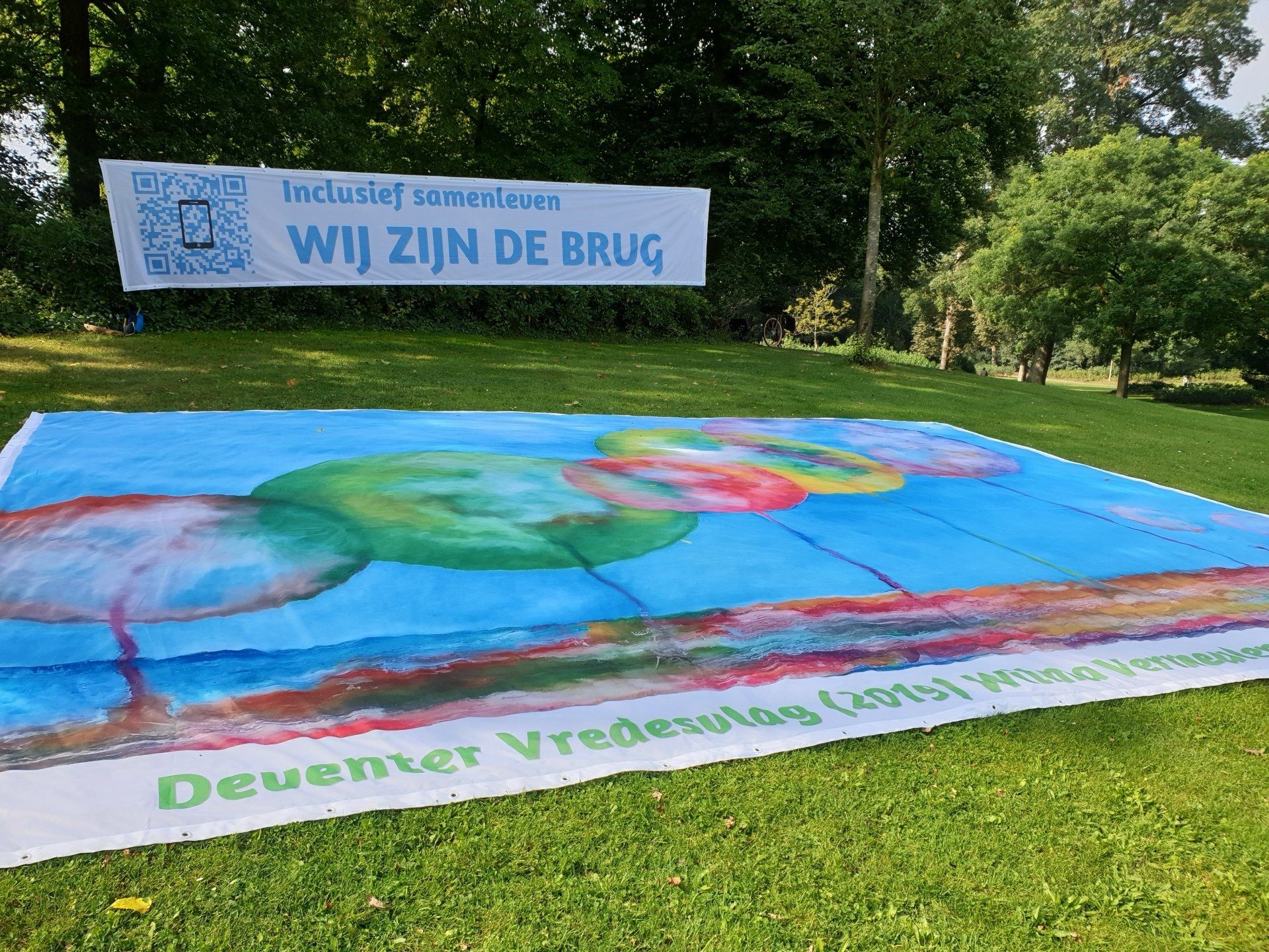 A large, painted banner on a grassy park lawn featuring colorful circles and text reading