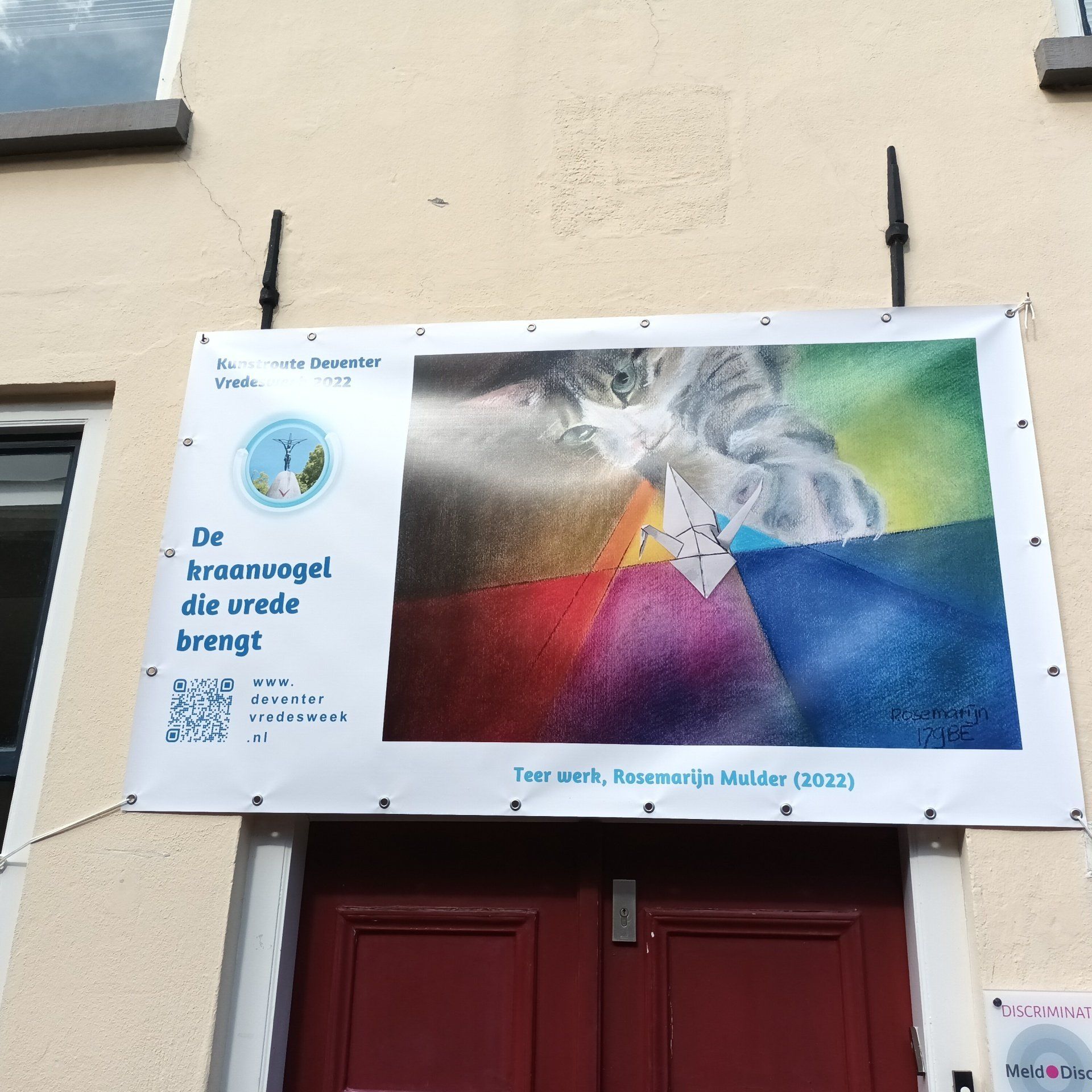 A banner above a door featuring a cat looking at an origami crane, with the text