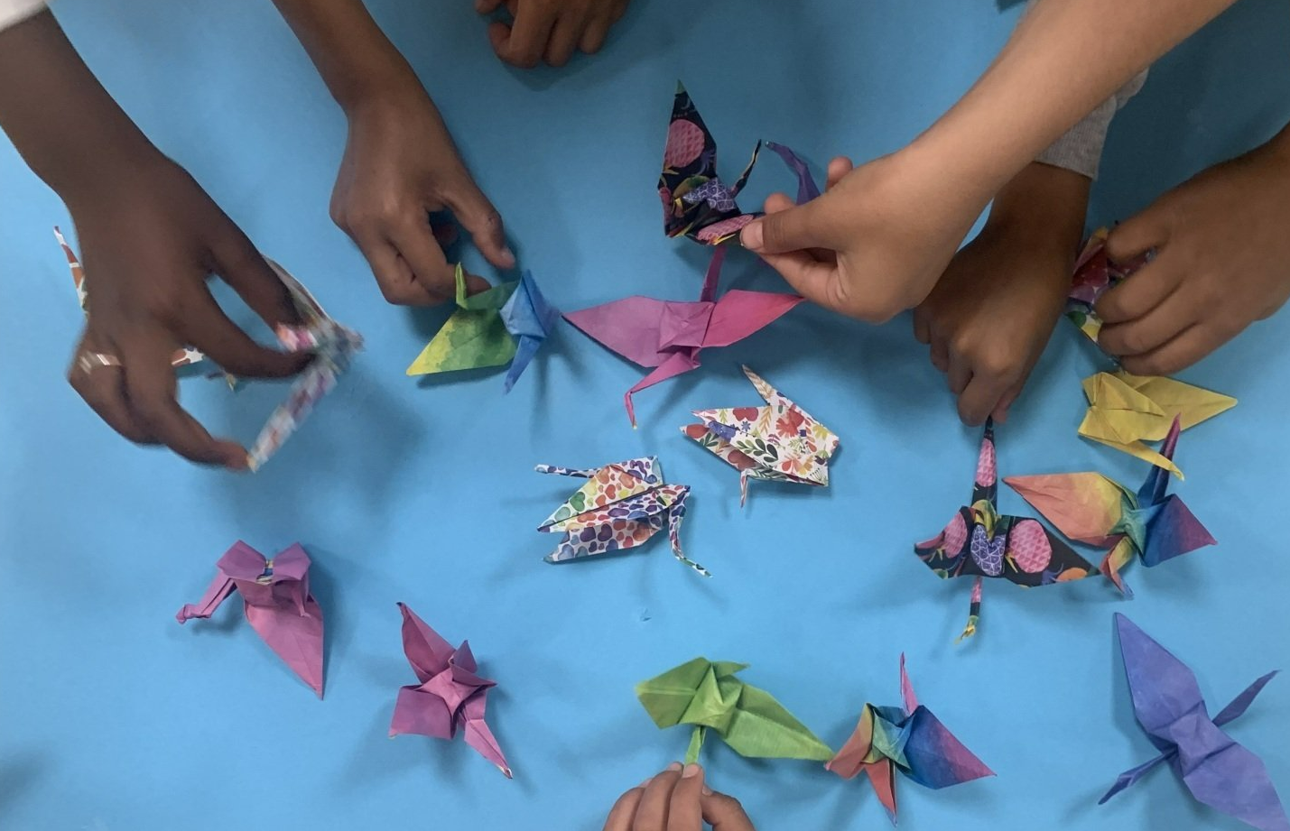 Handen schikken kleurrijke origami-kraanvogels op een blauwe ondergrond.