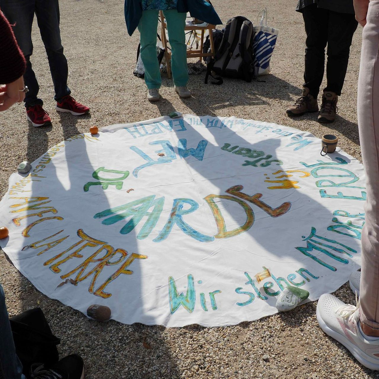 Een groep mensen staat rond een rond wit doek op de grond met daarop het woord