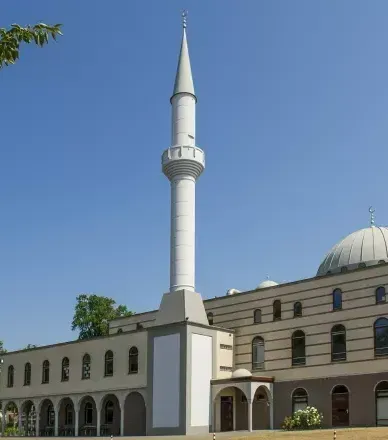 Een witte minaret verrijst naast een moskee met een koepeldak en boogvensters onder een helderblauwe hemel.
