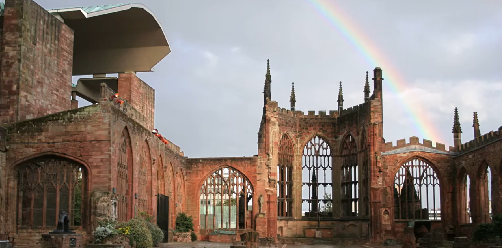 Een regenboog boog zich over de stenen ruïnes van de oorspronkelijke structuur van de kathedraal van Coventry tegen een bewolkte hemel.