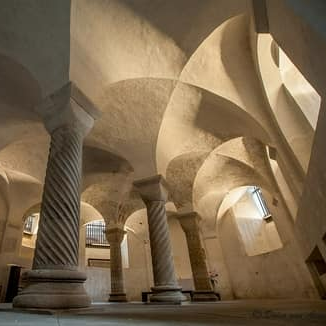 Spiraalvormige stenen zuilen ondersteunen hoge, gewelfde plafonds in een schemerig verlichte, oude stenen crypte of kapel.