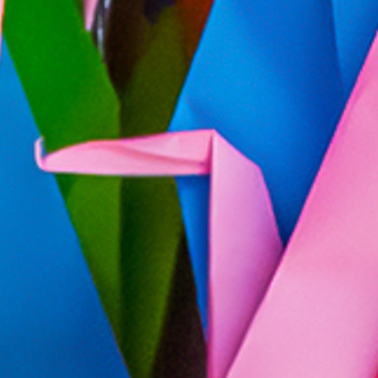 Close-up van kleurrijk origamipapier, gevouwen tot ingewikkelde, abstracte geometrische vormen in levendig blauw, groen en roze.