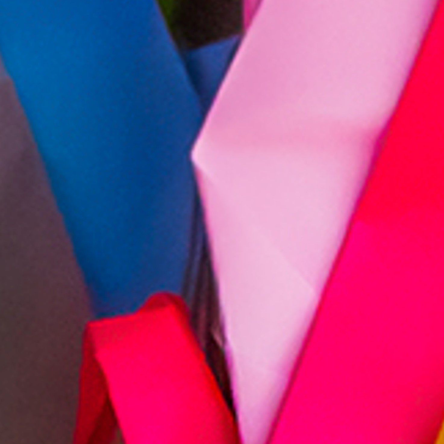 Felgekleurde, gevouwen stoffen vormen in blauw, roze en rood, die abstracte geometrische lagen creëren.