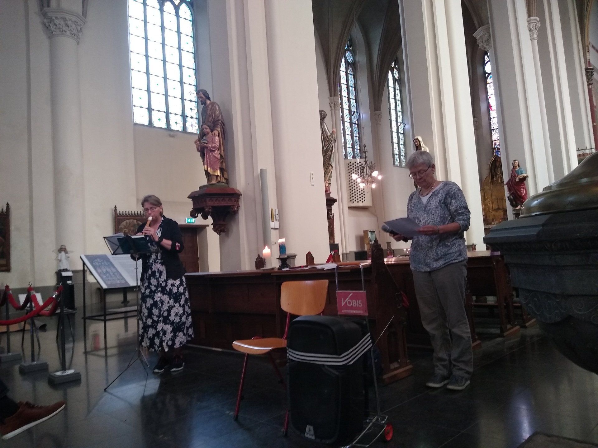 Twee mensen staan vooraan in een kerk, de een leest voor uit een document en de ander houdt een klein voorwerp vast.