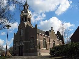 Een bruine bakstenen kerk met een centrale klokkentoren onder een blauwe hemel met witte wolken.