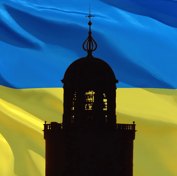 Een silhouet van een kerktorenspits tegen een achtergrond van de golvende, blauw-gele Oekraïense vlag.