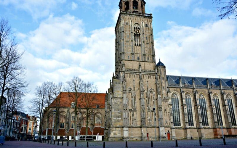 Een grote gotische kerk in Zutphen, Nederland, met een opvallende stenen toren en een gedeelte met een rood pannendak.