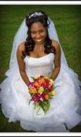 Bride in a white gown sitting outdoors, smiling and holding a colorful bouquet.