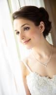 Woman in a white dress near a window, softly smiling and looking outside