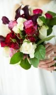 Bouquet of red, white, and pink roses held by hands in front of a white dress